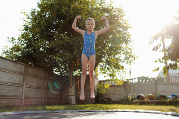 little sports girl jumps on a trampoline. Outdoor shot of girl jumping on trampoline, enjoys jumping in home. happy summer vacation