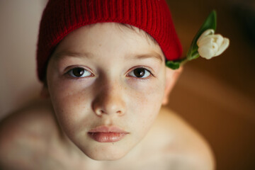 Hipster Cute Teenage boy with white tulip flower on ear in red knitted hat
