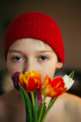 Cute Teenage boy with white tulip flower bouquet in red knitted hat