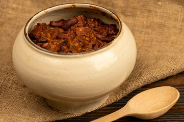 Stewed beans with meat in a small pot. A traditional rustic dish. Close-up, selective focus.