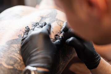man tattoo artist with black gloves with a tattoo machine drawing a tattoo on a man's body, close-up
