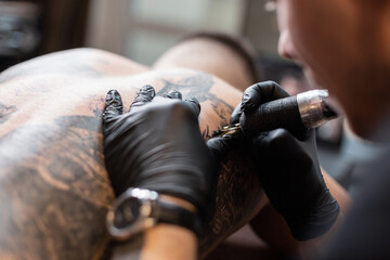 Close up of the tattoo machine. Tattooing. Man creating a picture on his back by a professional tattoo artist.