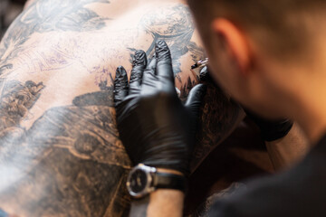 professional man with a tattoo machine stuffs a tattoo on a man's back, close-up. Tattoo artist in the workflow
