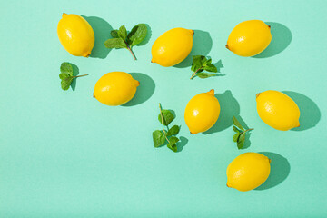 Fresh yellow lemons with mint on minimal blue background on bright sun light with hard shadows pattern summer background flat lay from above, citrus food composition, space for text