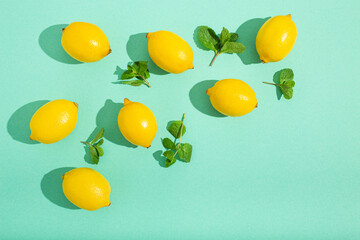 Fresh yellow lemons with mint on minimal blue background on bright sun light with hard shadows pattern summer background flat lay from above, citrus food composition, space for text