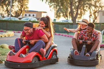 Group of multiracial friends having fun with go kart  - Young people with face mask on smiling and cheerful at mini car racing - Couples outside in double date - New lifestyle