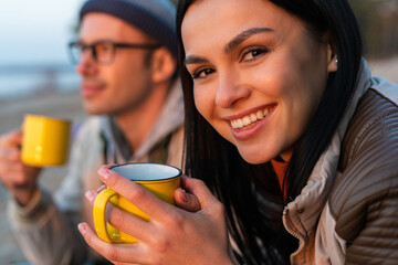 Two persons enjoying hot drinks while sitting at the nature. Portrait of the cheery brunette woman...
