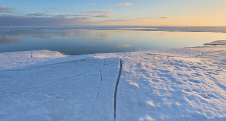 Coast of Gulf of Finland of the Baltic Sea in the end of winter: open water, before sunset, ice cracks.