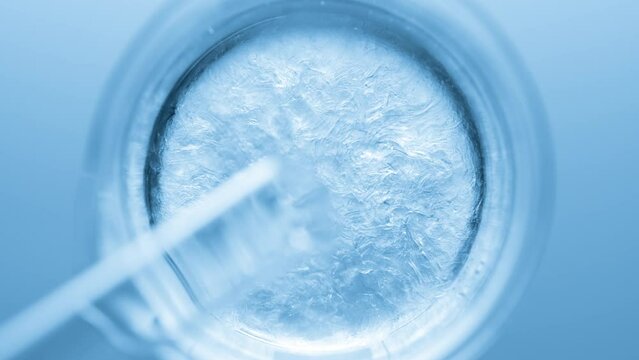 Top view macro shot of glycerin pouring into beaker with water creates ripples on its surface on pale blue background | Abstract body care cosmetics formulation concept