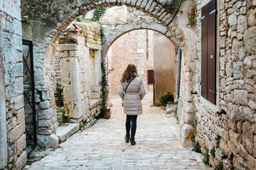 Girl wandering through the old, stone alleys of Istrian town of bale during cold weather, dressed in winter jacket
