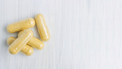 Yellow herbal capsules on white table, medication treatment, alternative medicine, close-up top view