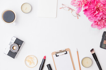 Fashion blogger workspace with blank paper clipboard, glasses, cup of coffee, pencil and pink peonies on a white table. Flat lay banner or shop header with makeup cosmetic products