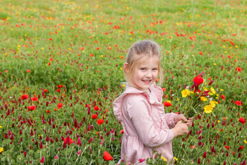 little blonde girl in a pink dress stands in a blooming field with a bouquet of flowers