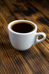 Close-up on black coffee in the white cup on the wooden  background. Location vertical.