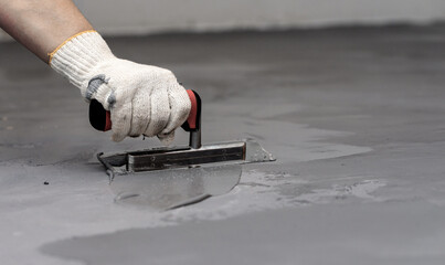 Close-up of a female worker applying microconcrete stucco to a floor with a trowel. - obrazy, fototapety, plakaty