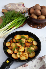 Fried potatoes are in a frying pan. Nearby are parsley and green onions.