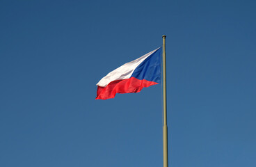 National flag of the Czech Republic, tricolor of red, white and blue. The Czech flag on a flagpole flutters in the wind against a blue sky.