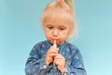 A small child found cosmetics from her mother and paint her lips with lipstick.