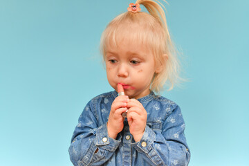 A small child found cosmetics from her mother and paint her lips with lipstick.