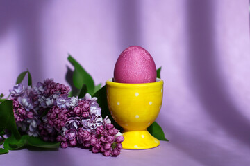 a bright purple easter egg and lilac flowers on a purple background. Easter decor.
