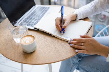 Close-up view of a woman's hands writing notes in a notebook. Girl working in a cafe