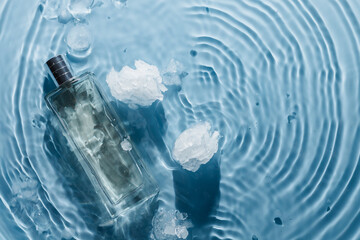 Perfume bottle on blue water wavy background with ice pieces. Fresh chilly water fragrance concept