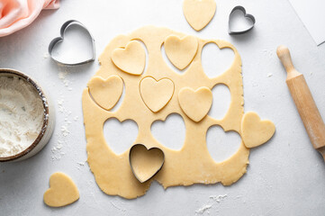 The process of cooking heart cookies. Top view of raw dough, rolling pin and baking cutters.