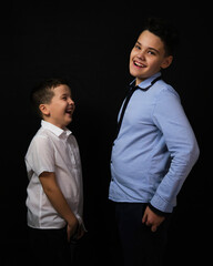 two boys on a black background are brothers. they look at each other.They smile and laugh.Big teeth.Looks at the camera