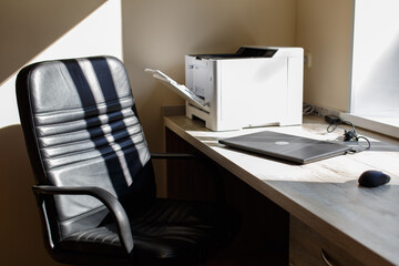 workplace in the office: desk, chair, laptop, printer close up in front of a sunny window . close laptop on desk in a office on background.