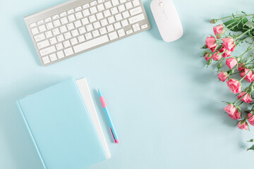 Female desktop, сomputer keyboard, notepad, rose flowers on pastel blue background. Valentine day concept. Flat lay, top view, copy space