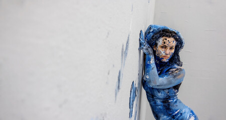 sexy artistically abstract painted adult woman in underwear, with blue and white, paint, stands seductively demanding in front of gray wall in studio and leaves color prints