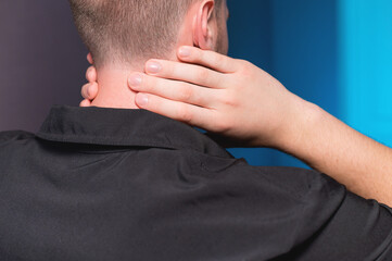 Fototapeta premium Close-up. A freelance man in a dark shirt has a sore neck after working for a long time, he massages his neck himself.