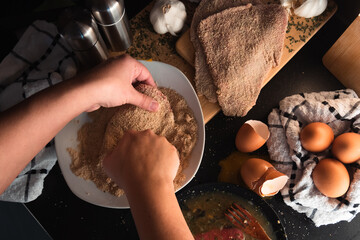 hands breading an escalope, ingredients in the background