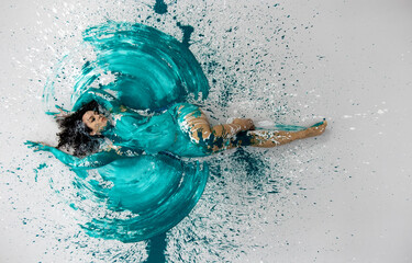 top view to expressive sexy woman lies elegant on the floor in turquoise blue color abstractly painted bodypainting woman on the splashed ground, spreads the paint in the form of angel wings