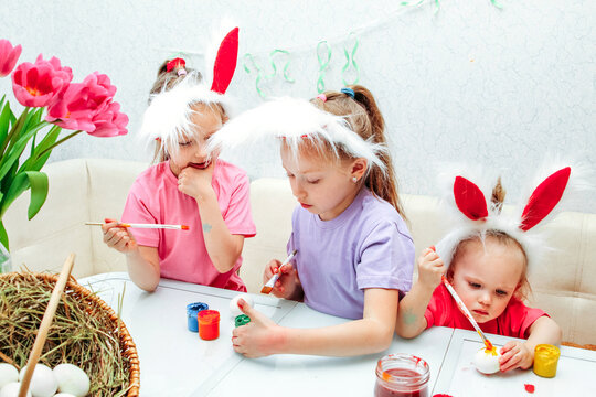 Three girls paint eggs with gouache. Preparation for the bright Easter holiday. Crafts for children at Easter for home decoration. Child girls are passionate about coloring eggs with paints