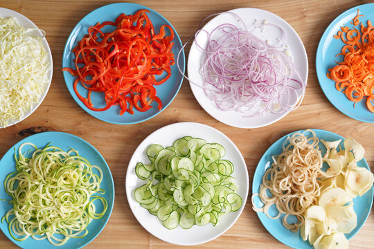 Vegetable spirals from a spiral cutter in plates on a wooden surface. Vegetarian pasta. Home cooking. Top view.