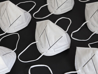 Many clean and unused KN95 white respirator dust masks are shown on display, set on a solid black background.