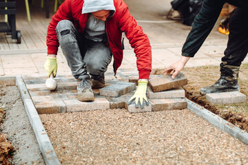 Close-up of construction worker installing and laying pavement stones on terrace, road or sidewalk....