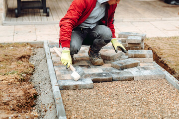Portrait of industrial worker Laying grey concrete paving slabs in house courtyard on gravel...
