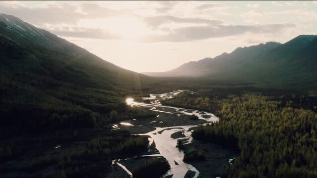 Aerial of Alaska landscape between a valley following a river as the sun begins to set.