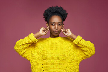 Stubborn stylish serious african american young girl sticking plug ears by fingers not listening,...