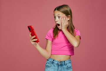 Shocked child girl hold phone surprised by unexpected news, shock content in social media on pink...