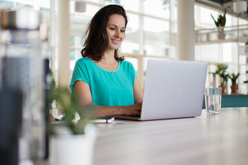 happy smiling remote working dark haired woman typing on laptop or notebook in casual outfit...
