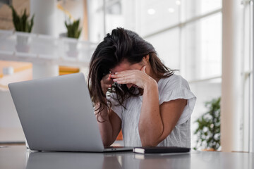sad depressed remote working woman sitting disappointed with headache infront of a laptop or...