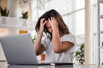 sad depressed remote working woman sitting disappointed with headache infront of a laptop or...