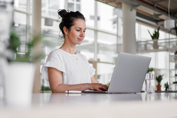 happy smiling remote working dark haired woman typing on laptop or notebook in casual outfit...