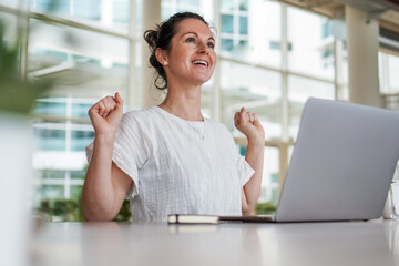 happy joyful successful remote working woman cheerful with fists infront of laptop or notebook in...