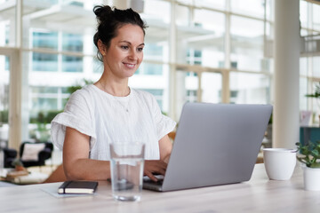 happy smiling remote working woman talking to laptop or notebook in casual outfit sitting on her work desk in her modern loft living room home office having a video chat