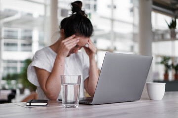 sad depressed remote working woman sitting disappointed with headache infront of a laptop or...