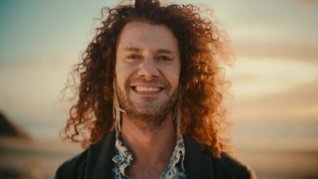 Portrait of a Happy Young Adult Man with Long Curly Hair, Wearing Earrings and Nose Ring, Posing for Camera. Handsome Multiethnic Caucasian Male Charmingly Smiling. Warm Color Edit.